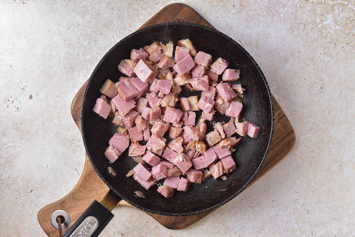 chunks of meat frying in black frying pan sitting on wooden board.