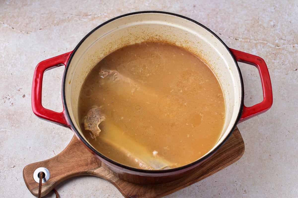 pork ribs cooking in meat broth in large pot with red handles.