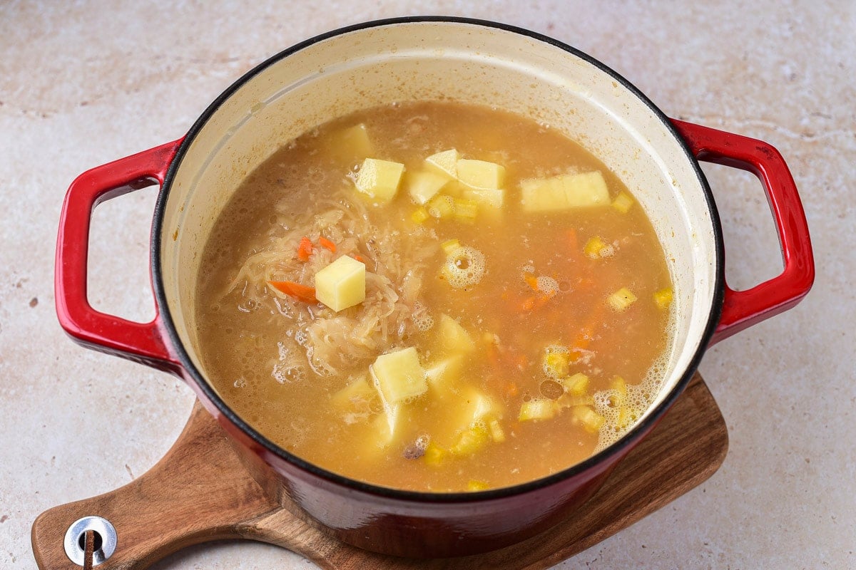 chunks of raw potato and other vegetables cooking in meat broth in pot.