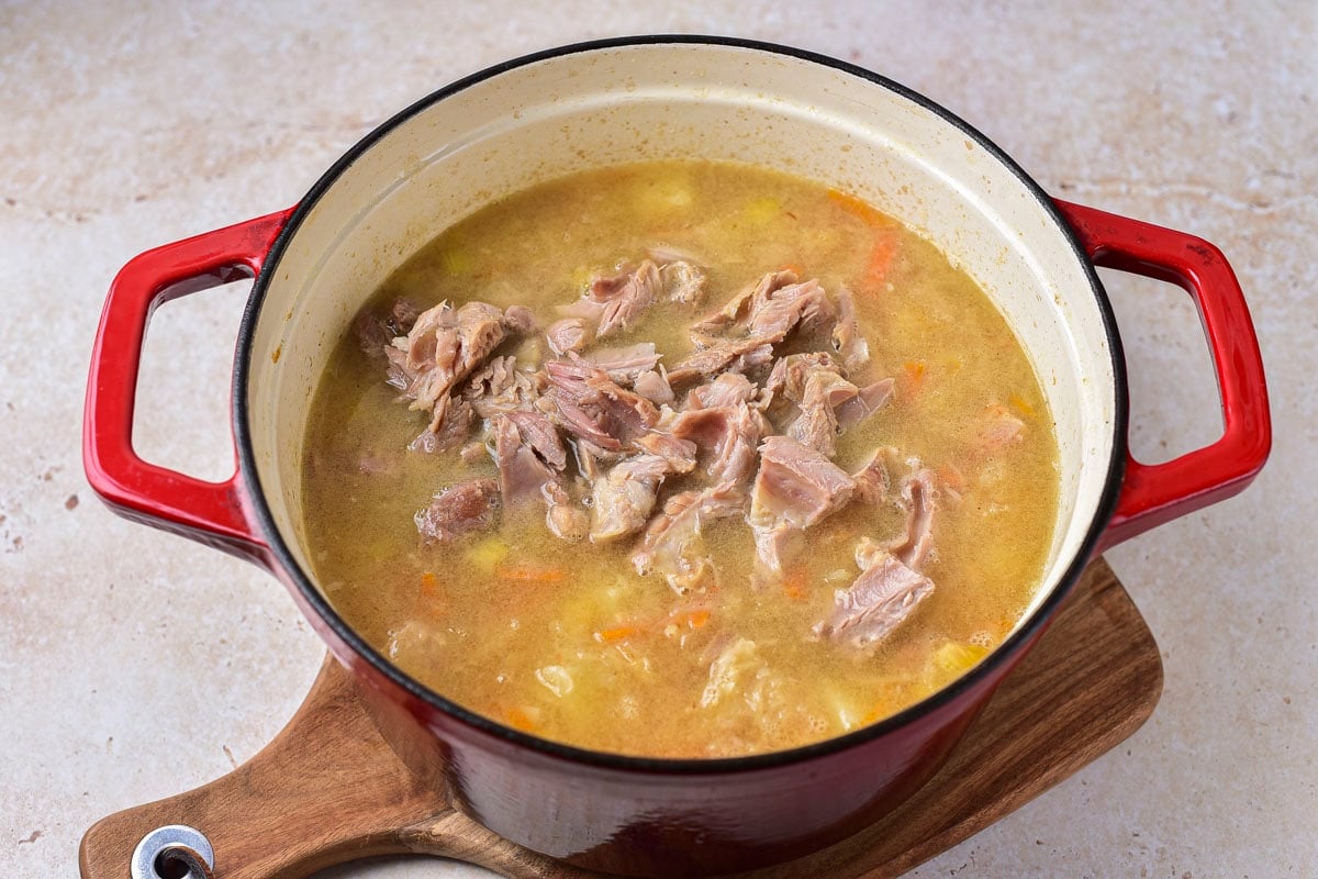 pieces of shredded meat on top of broth in large red pot of sauerkraut soup.