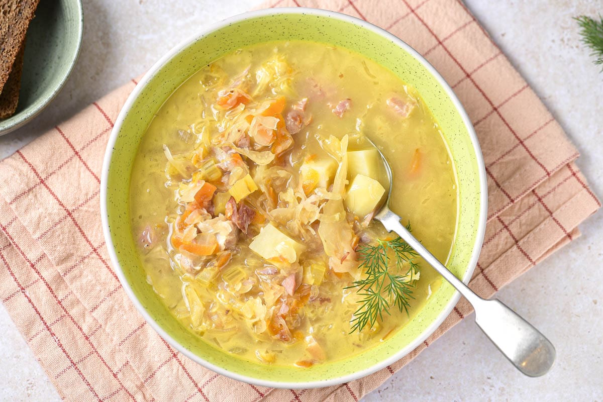 green bowl of sauerkraut soup with silver spoon sticking out resting on folded cloth.