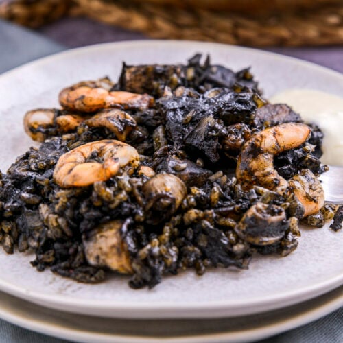 plate of squid ink paella on plates with fork beside.