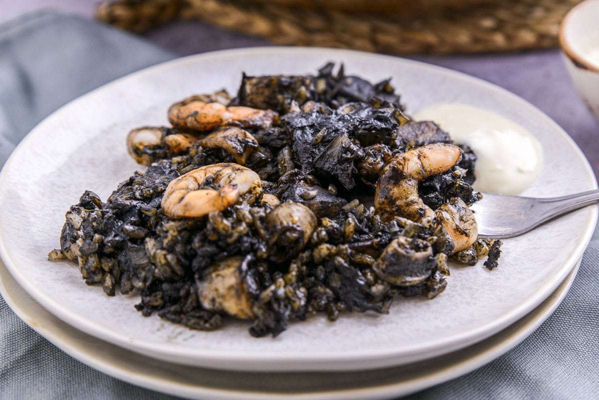 plate of squid ink paella on plates with fork beside.