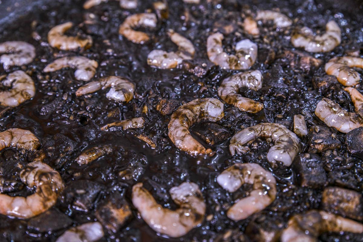 raw prawns sitting on top of black rice dish in large pan.
