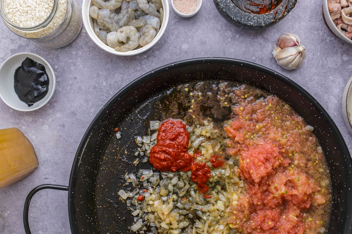 frying onions grated tomato and red pepper paste frying in large black flat pan.