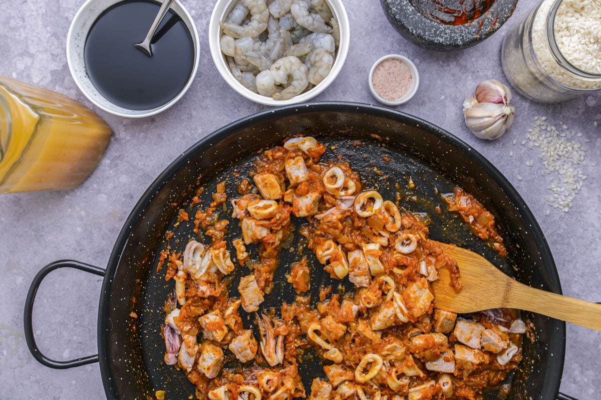 large black pan frying seafood pieces in tomato mixture.