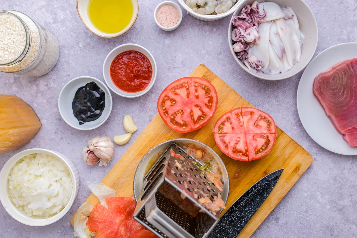 two large tomato halves beside grater sitting on wooden cutting board.