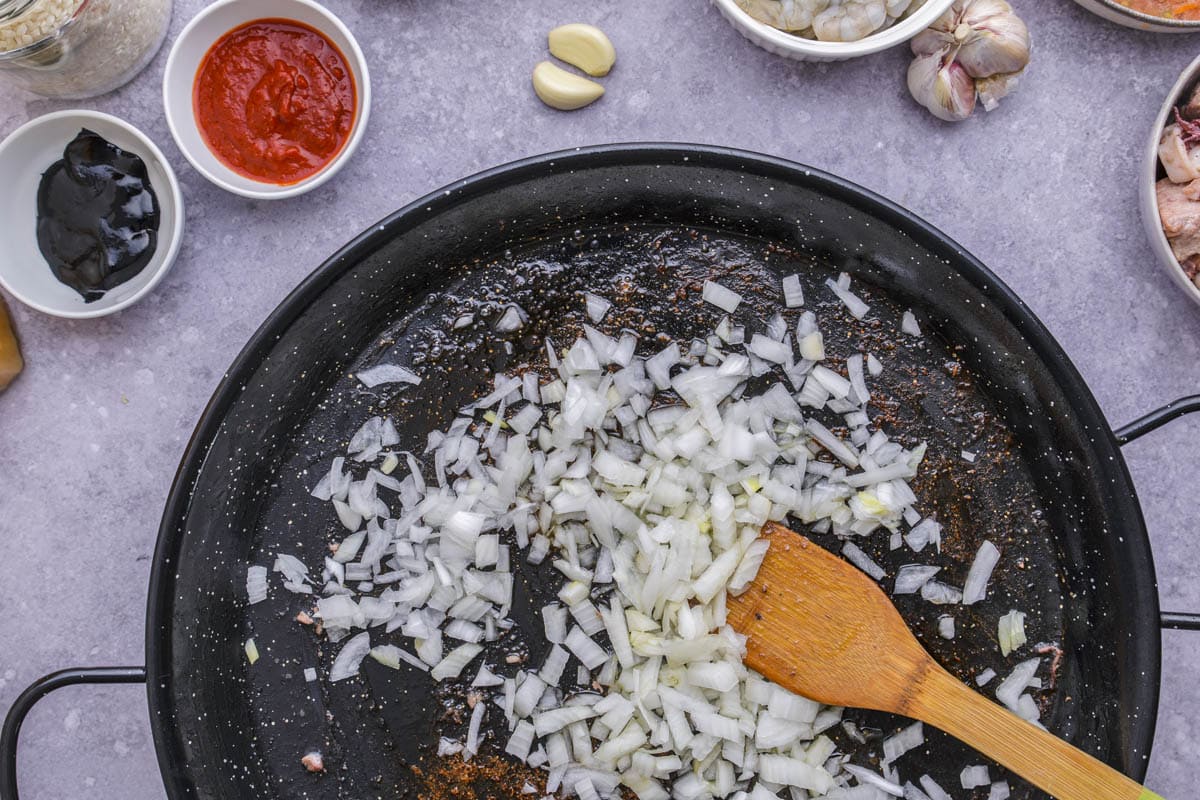 chopped onions frying in large black pan with wooden spatula stirring them.