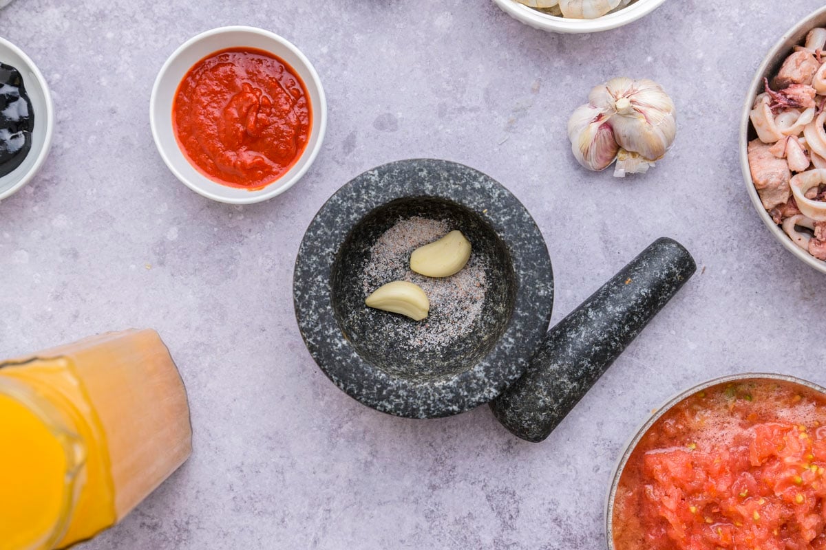 two garlic cloves in black mortar and pestle sitting on counter top.