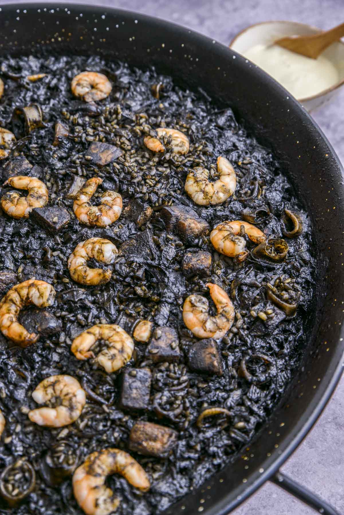 large flat black pan filled with cooked black rice seafood paella.