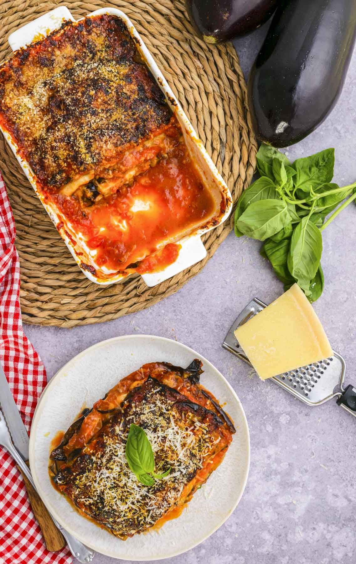 baking dish of eggplant parmesan cut into slices with one slice on white plate nearby on counter.