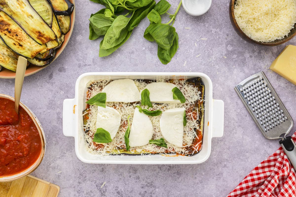 fresh basil and slices of mozzarella layered in white baking dish on counter.
