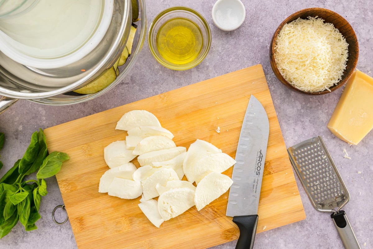 slices of fresh mozzarella on wooden cutting board with knife beside.