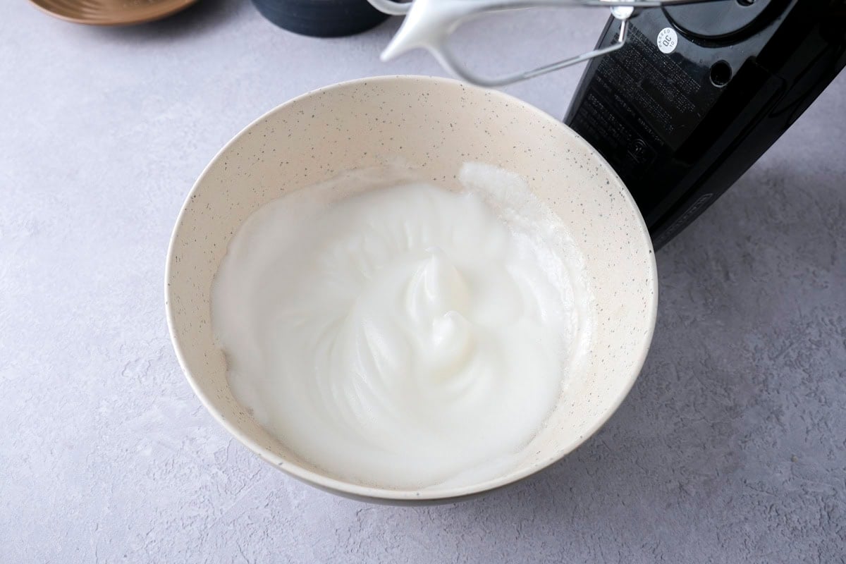 egg whites whipped in white mixing bowl on counter.
