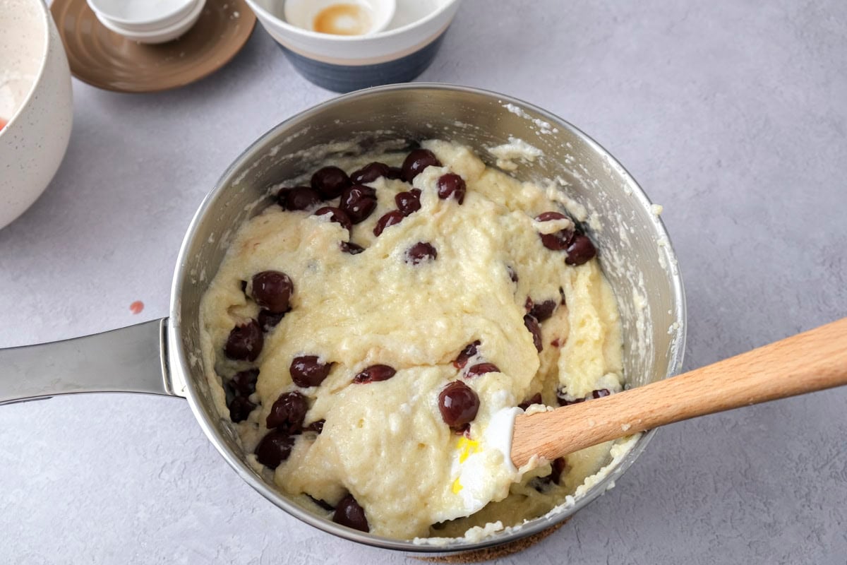 cherries folded with spatula into semolina mixture in silver pot on counter.