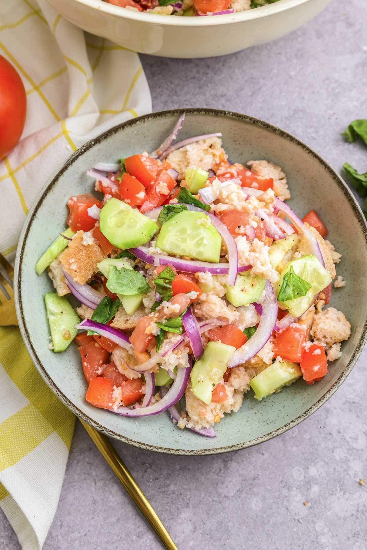 colourful italian bread salad in bowl with golden fork beside on counter.