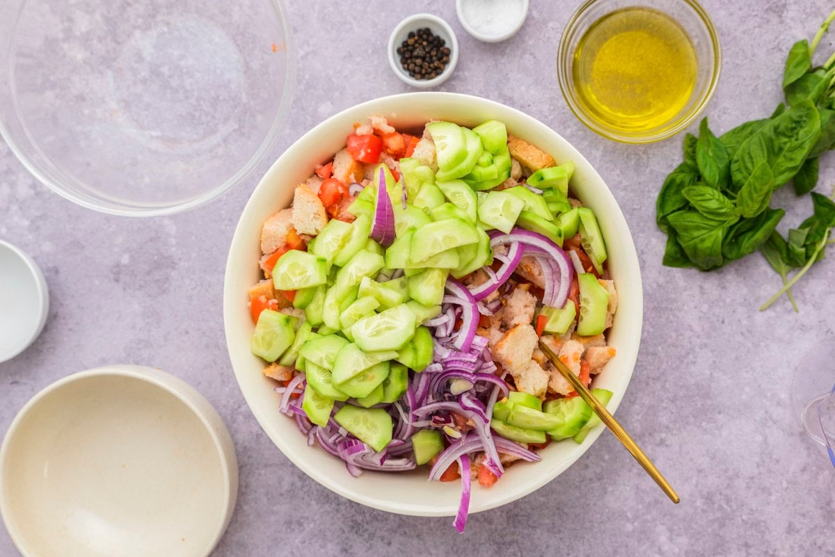 white mixing bowl of chopped vegetables with gold spoon sticking out on counter.