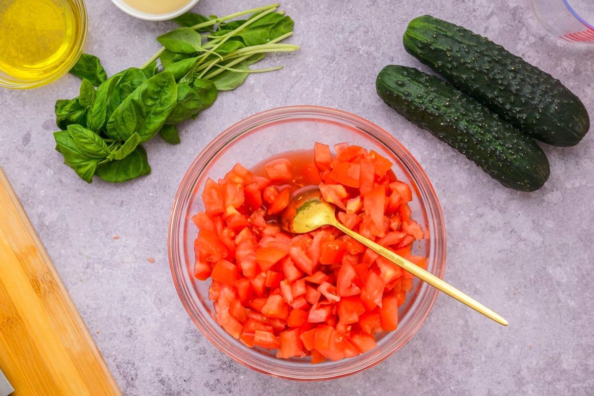clear mixing bowl of diced tomatoes with golden spoon sticking out.