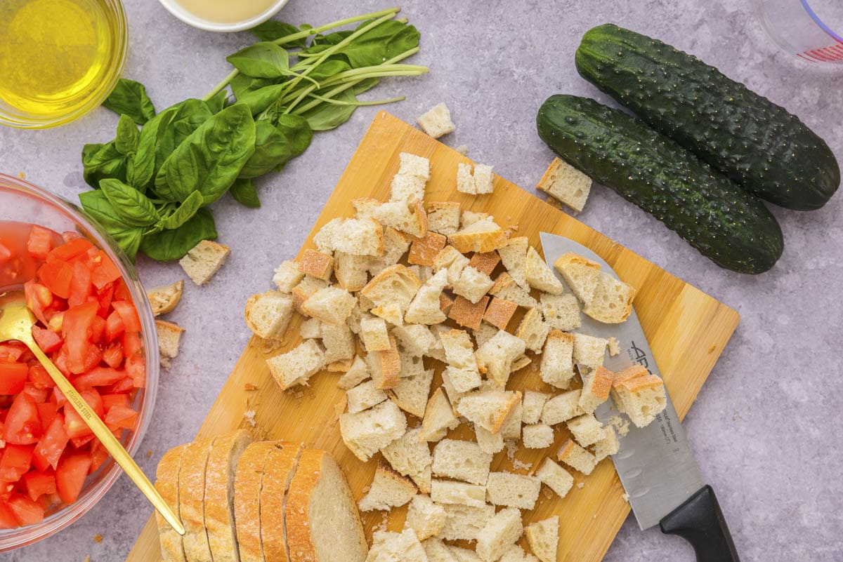 stale bread diced into cubes on wooden cutting board with knife beside.