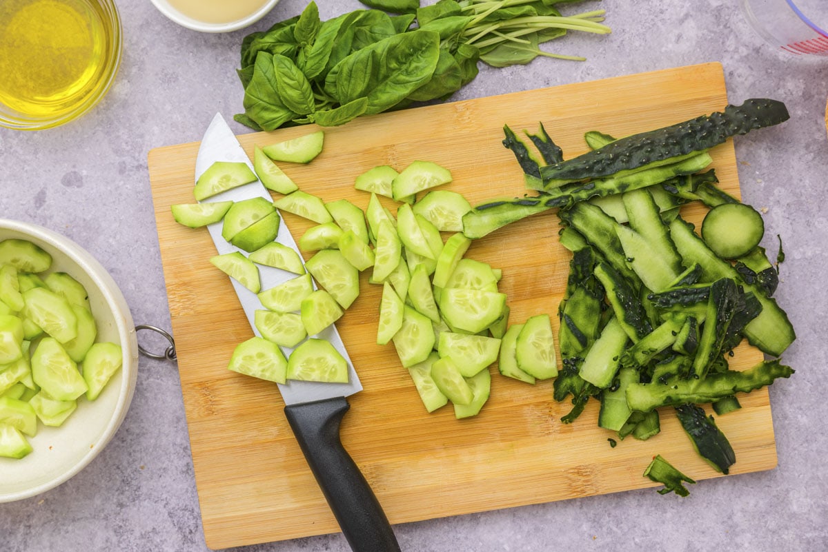 cucumbers chopped into pieces on wooden cutting board with knife beside.