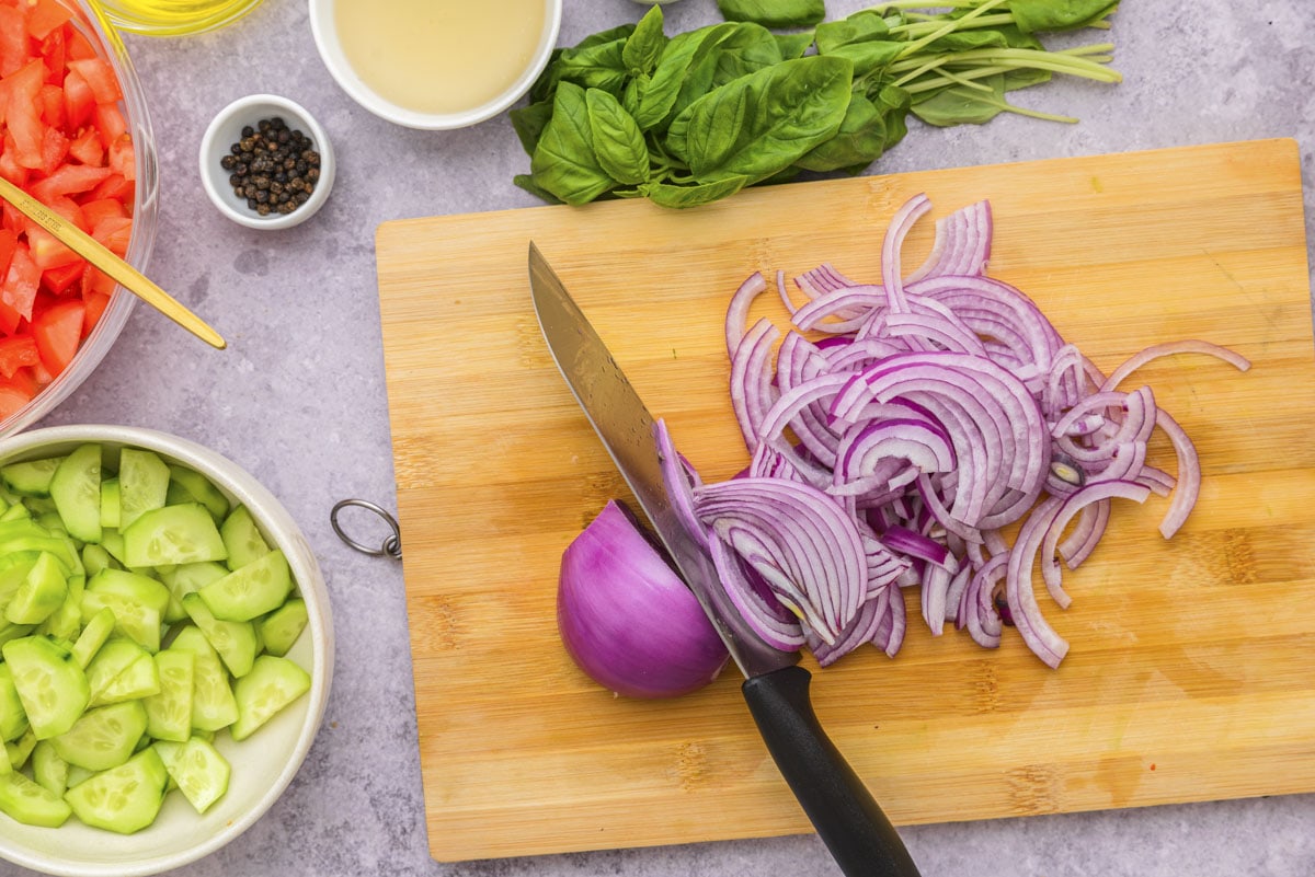 red onion cut into slices on wooden cutting board with knife beside.