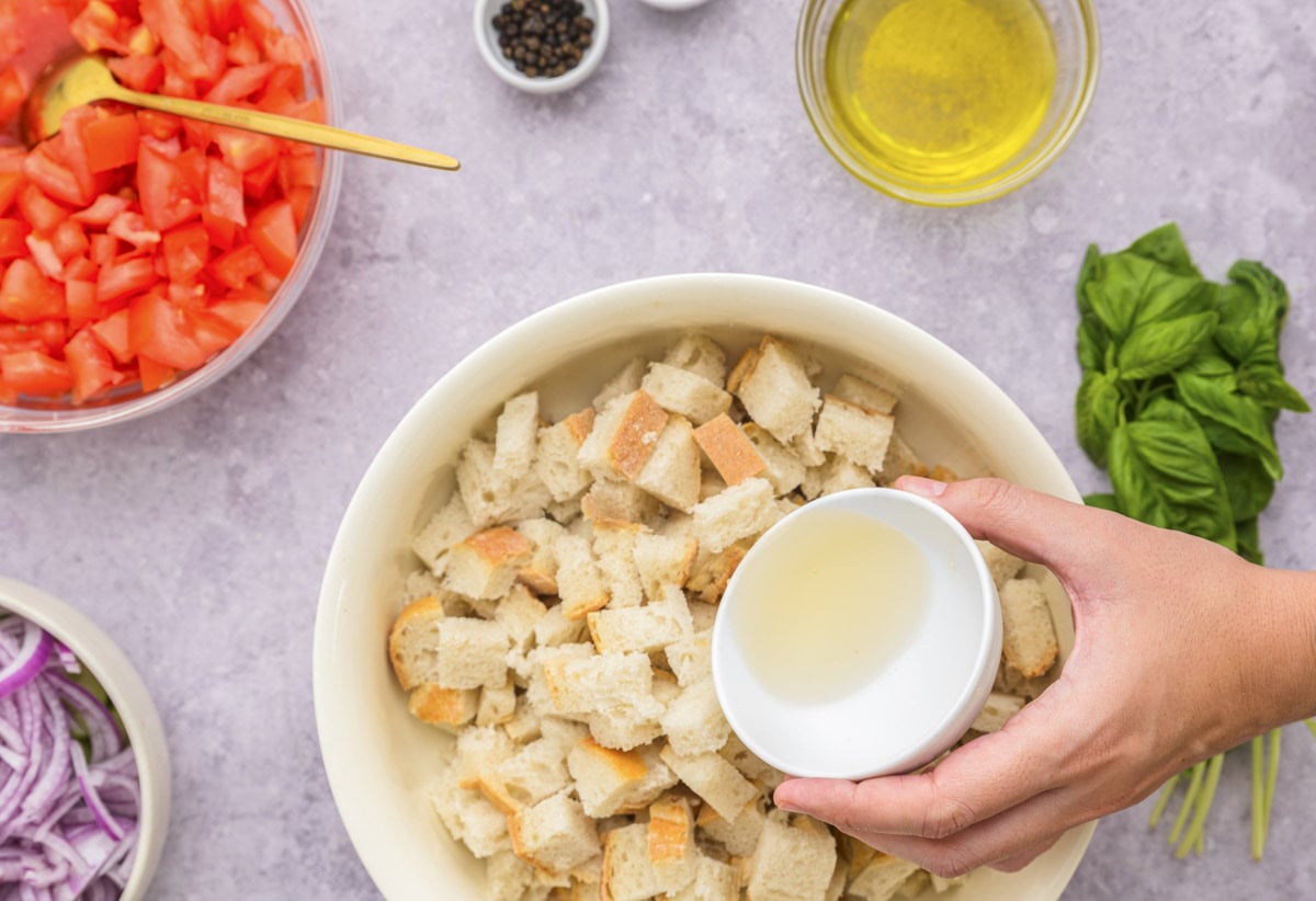 hand pouring ramekin of liquid into bowl of stale cut bread.