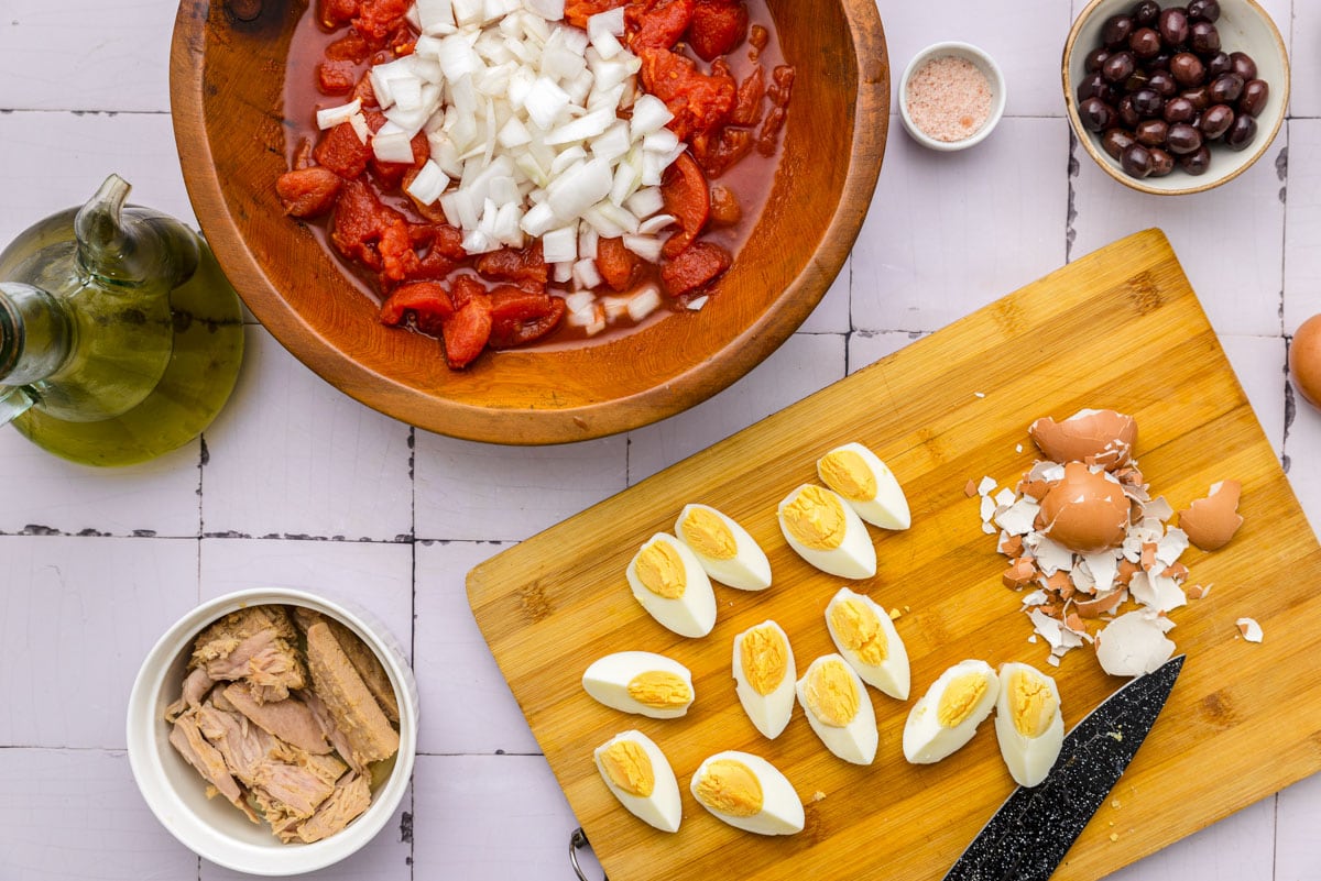 hard boiled eggs cut up on wooden cutting board sitting beside wooden bowl of tomatoes.