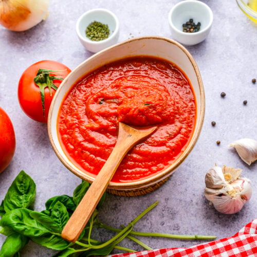 bowl of red marinara sauce sitting on counter with wooden spoon sticking out.
