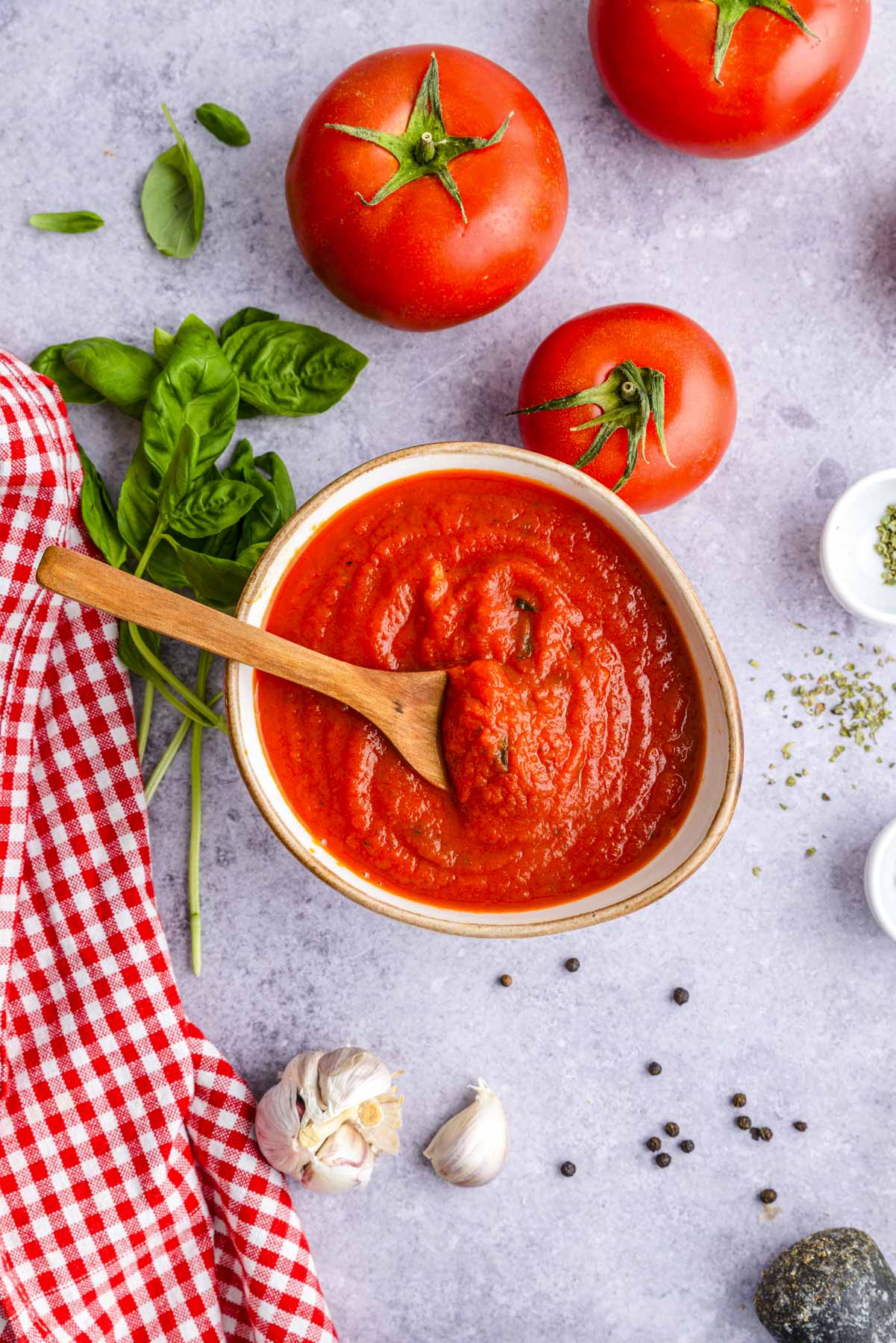 freshly made marinara sauce in white bowl on counter with wooden spoon sticking out.