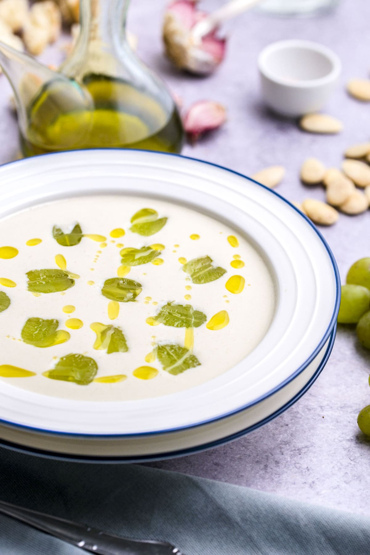 bowl of white spanish gazpacho on counter topped with olive oil and grapes.