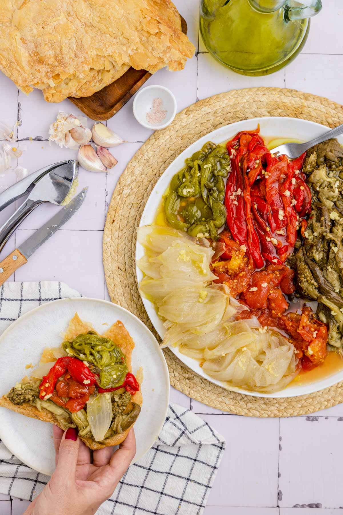 hand holding bread with roasted vegetables beside large plate of roasted vegetables.