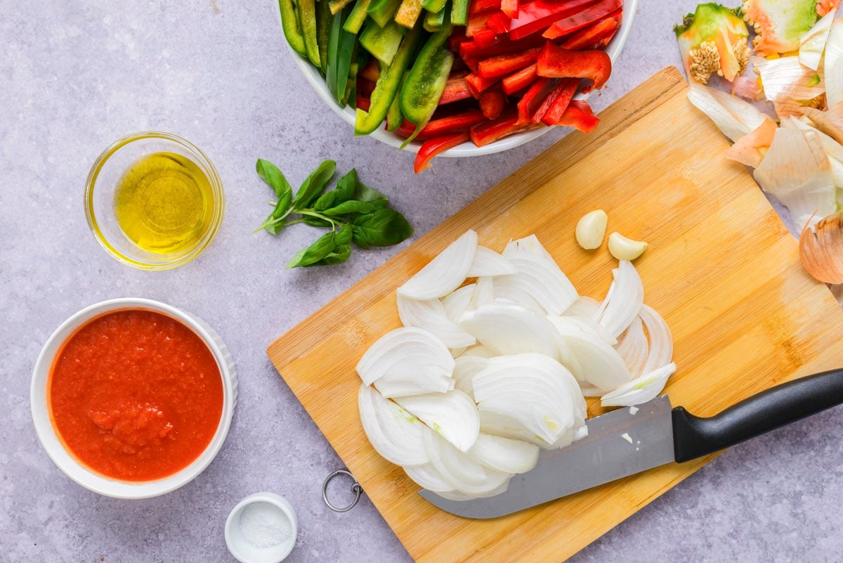 white onion sliced into pieces on wooden cutting board with knife beside.