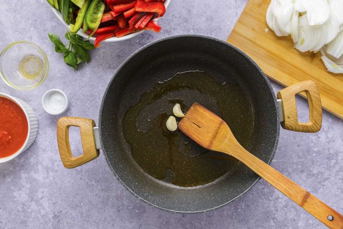 garlic cloves roasting in pan with wooden spatula moving them.