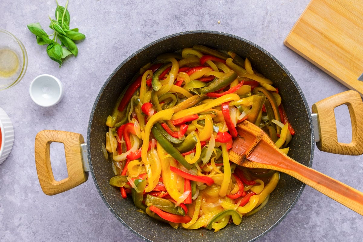 slightly cooked bell pepper pieces in black frying pan on counter.
