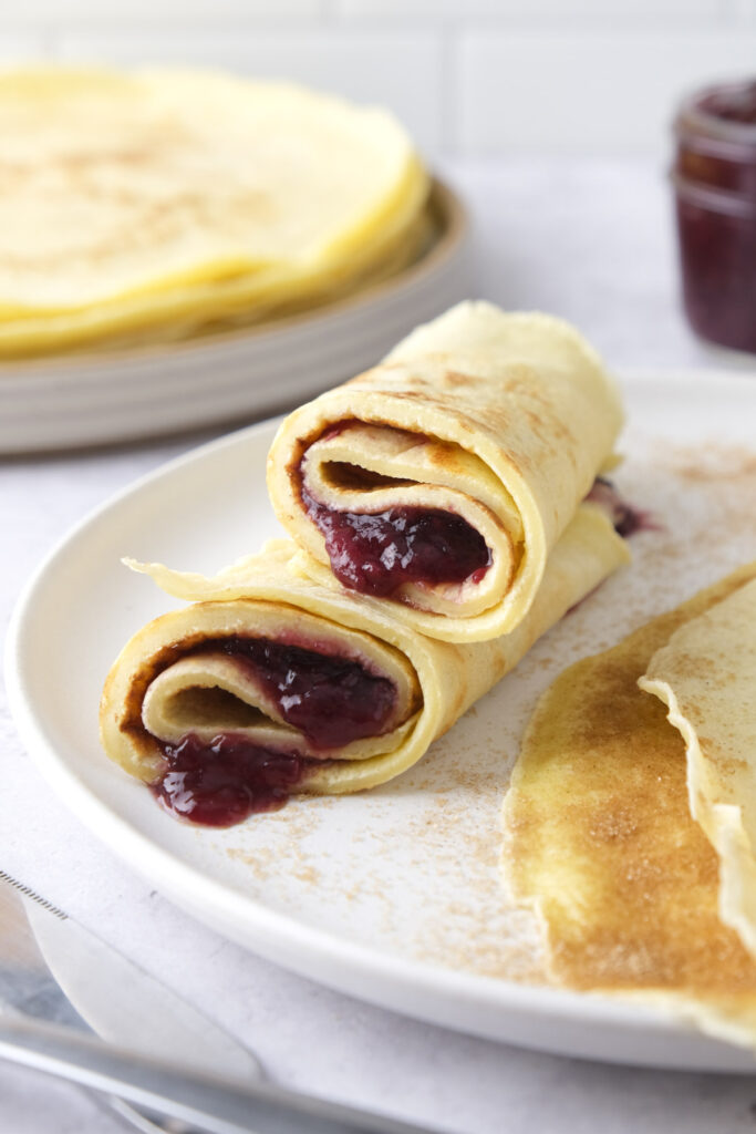 rolled german pancakes filled with jam on plate with more pancakes around.