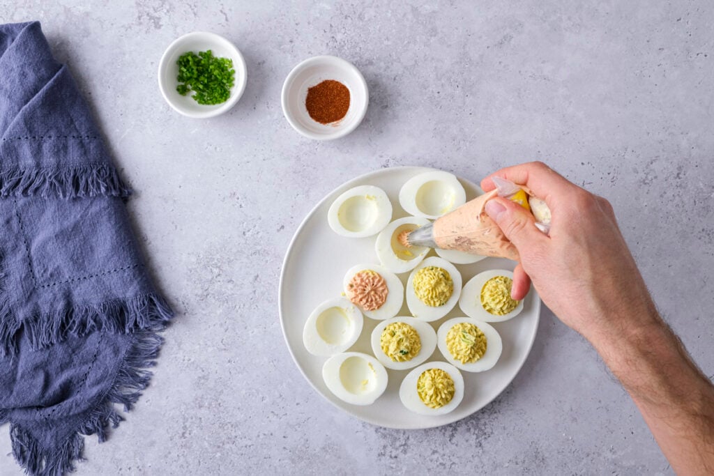 hand piping egg yolk mixture into deviled eggs on counter.