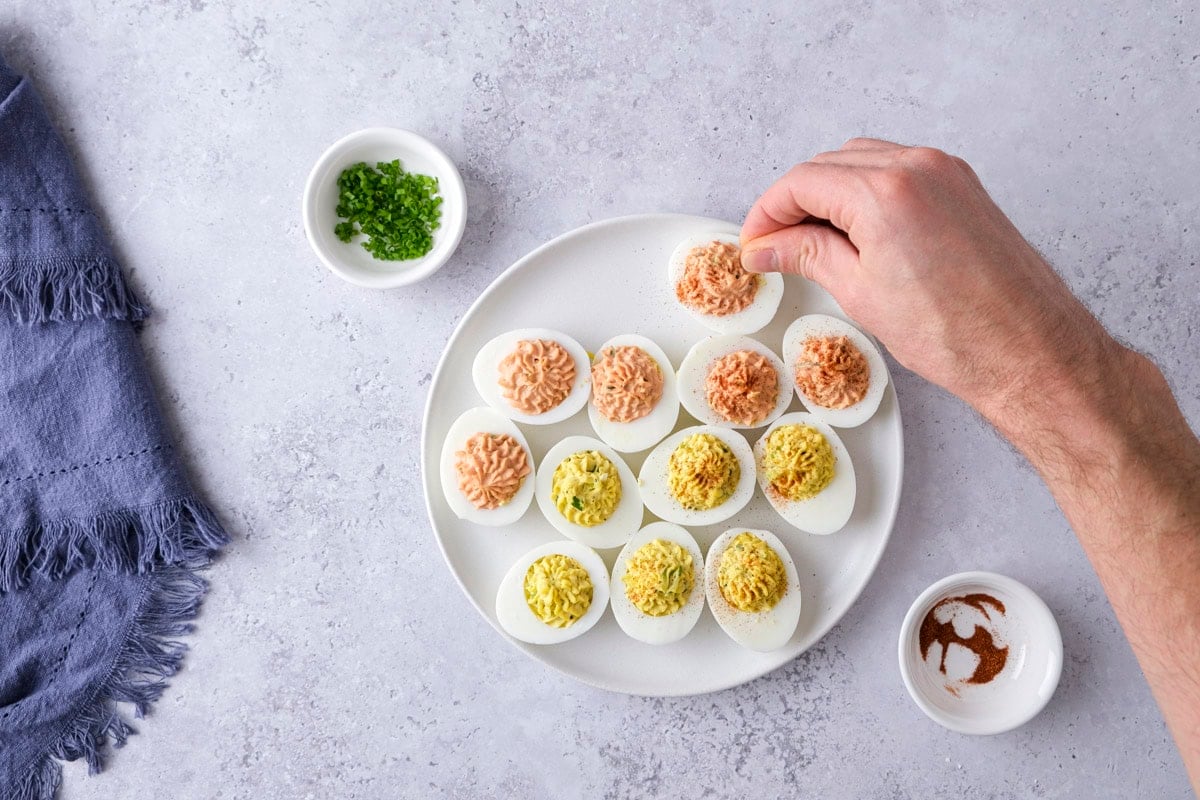 hand adding paprika onto deviled eggs on plate sitting on counter.