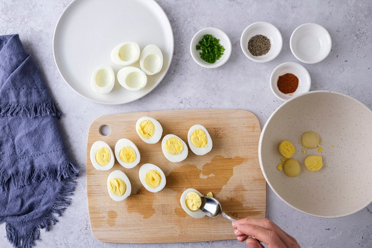 spoon removing egg yolk from cooked egg on counter with ingredients around.