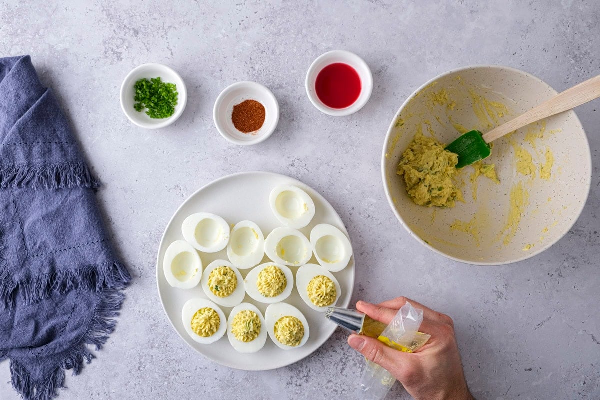 hand piping egg yolk mixture into deviled egg halves.