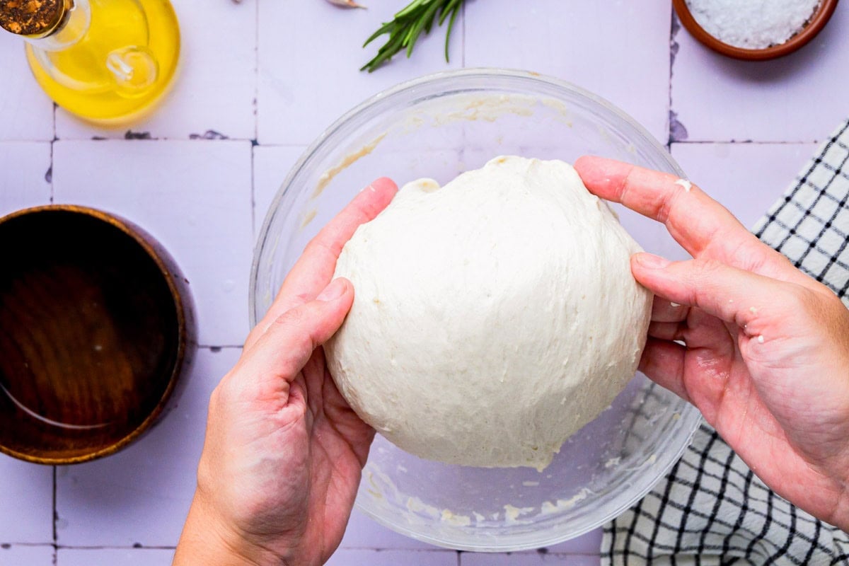 hand making a round lump with focaccia dough with counter top around.