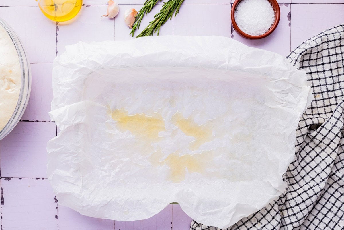 olive oil sitting on top of parchment paper lined pan on counter.