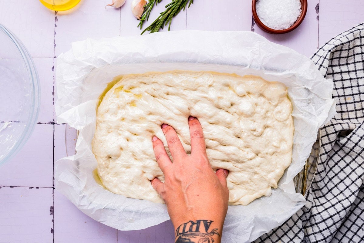 hand pressing down into focaccia dough in pan.