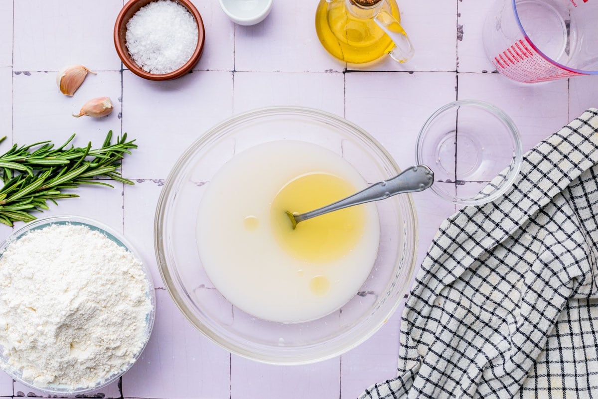 salt and olive oil added to yeast water mixture in bowl on counter top.