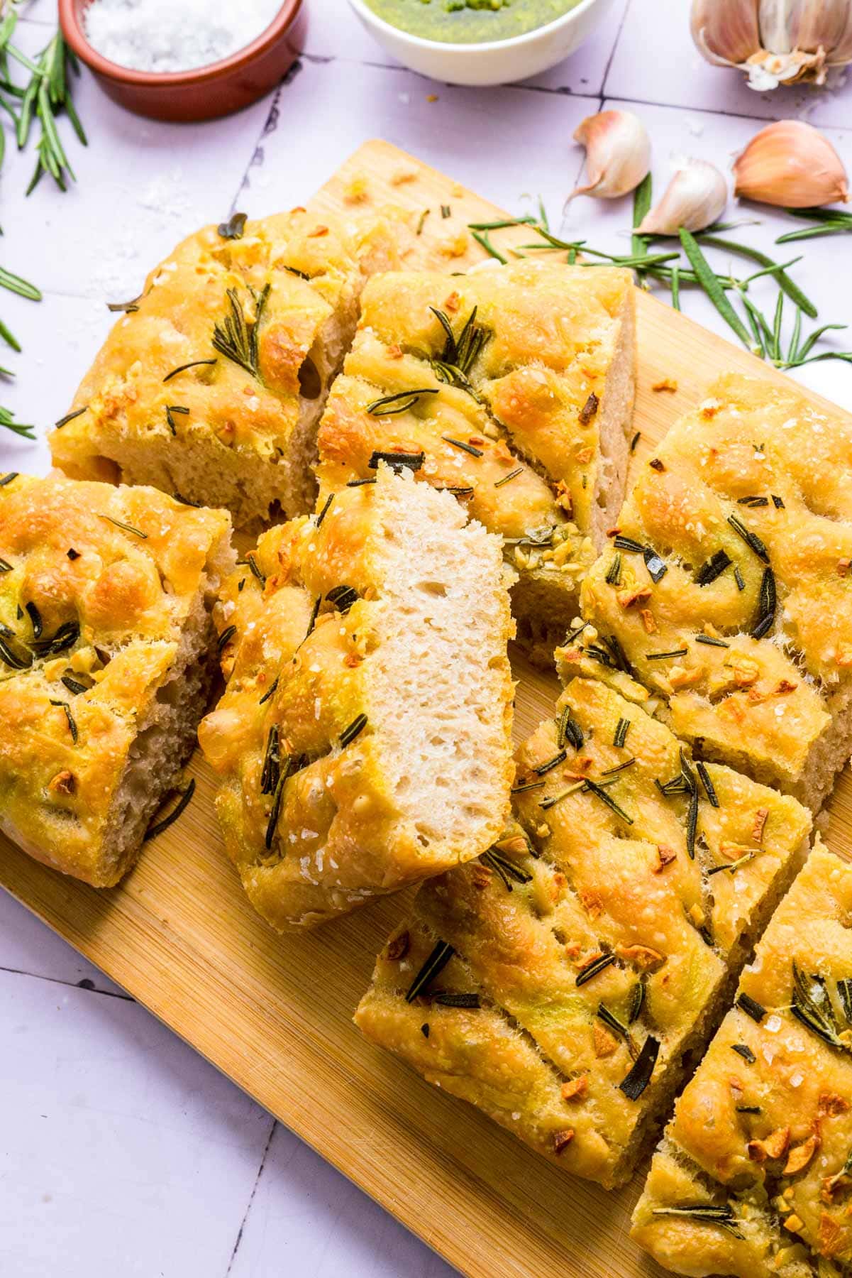 large rosemary focaccia cut into slices on wooden board.