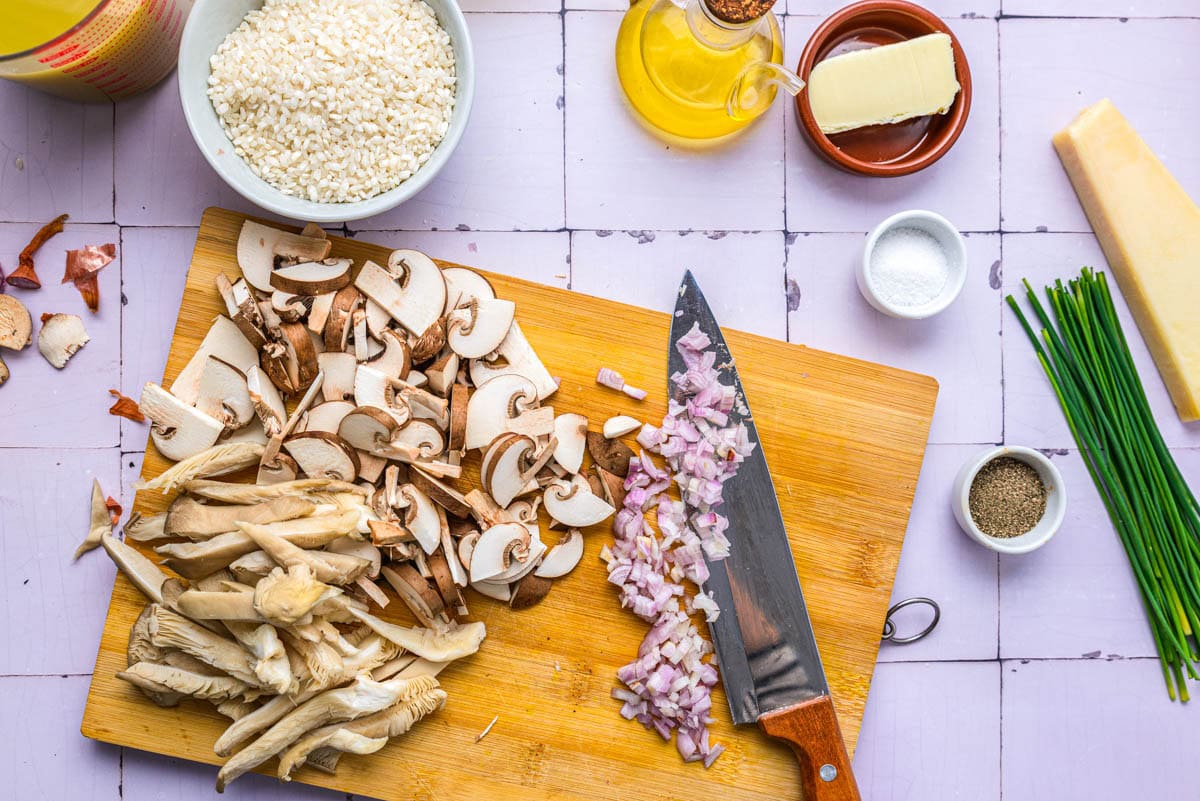 knife cutting shallots and mushrooms on wooden cutting board.