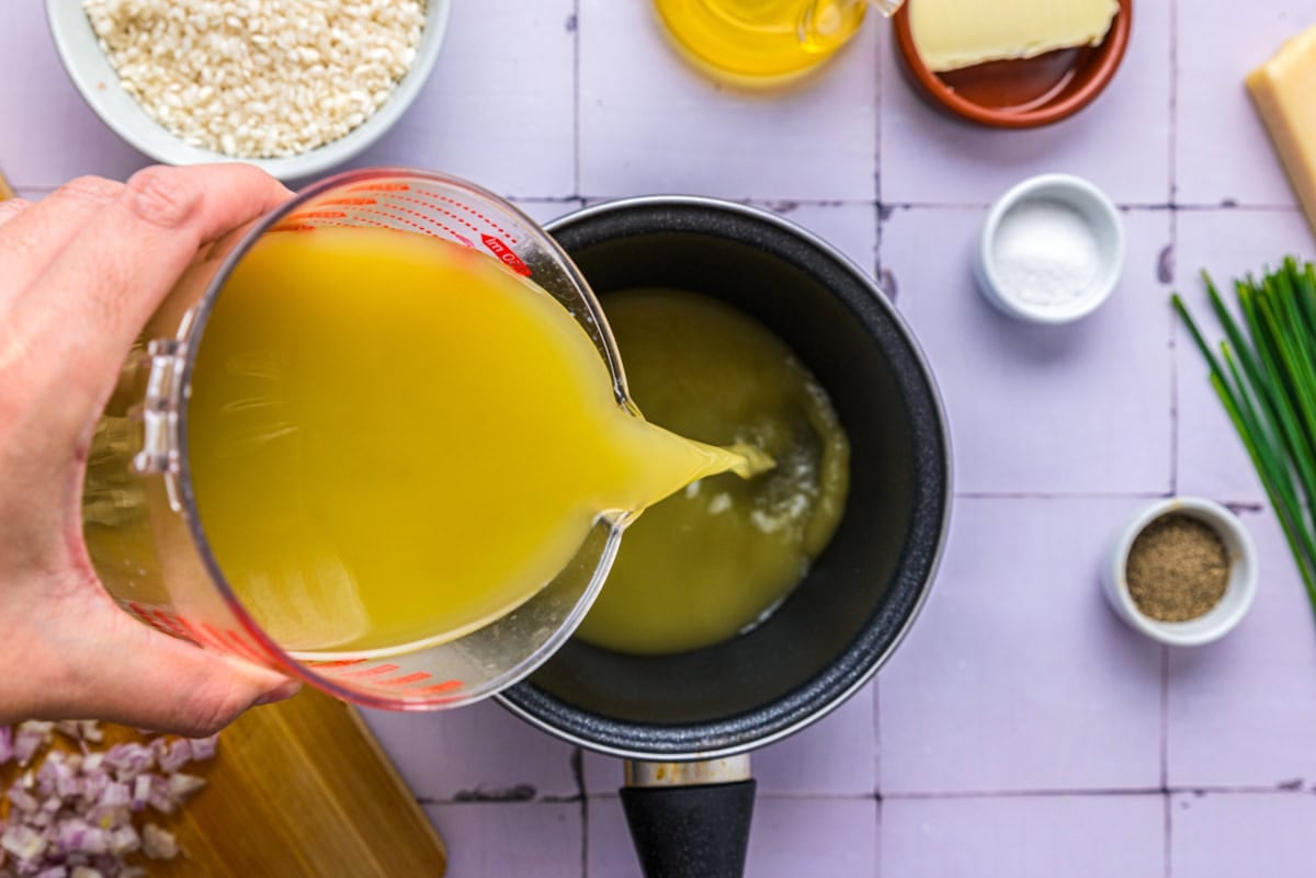 hand pouring vegetable broth into a sauce pan on counter.