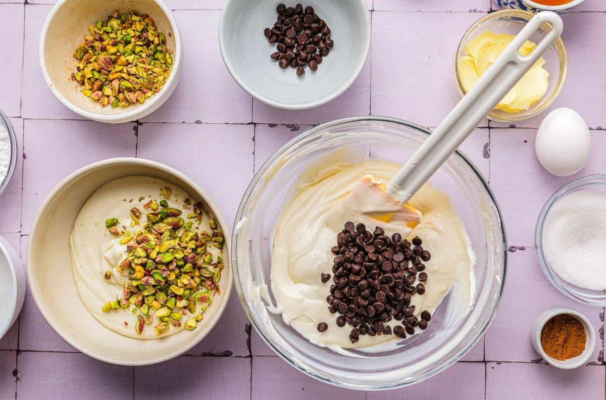 chocolate chips and pistachios being added to creamy cheese filling in bowls.