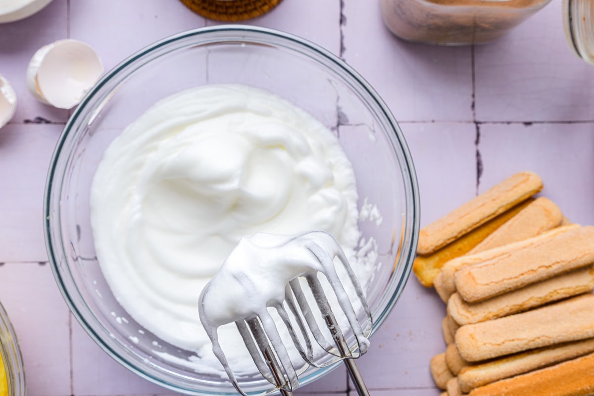 thick and fluffy whipped egg whites in glass bowl on counter.