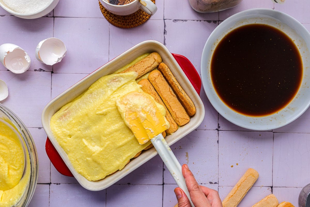 hand spreading another layer of sweet cheese mixture on ladyfingers.