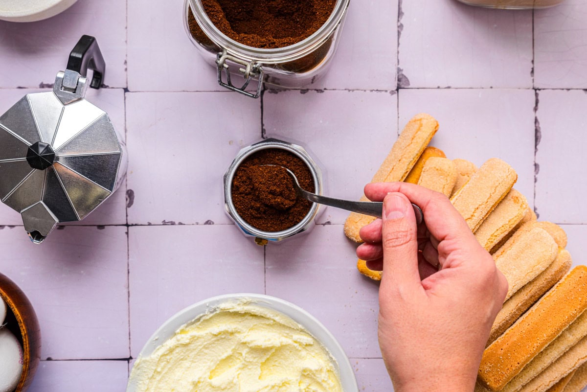 ground espresso beans held in spoon by hand above a counter.